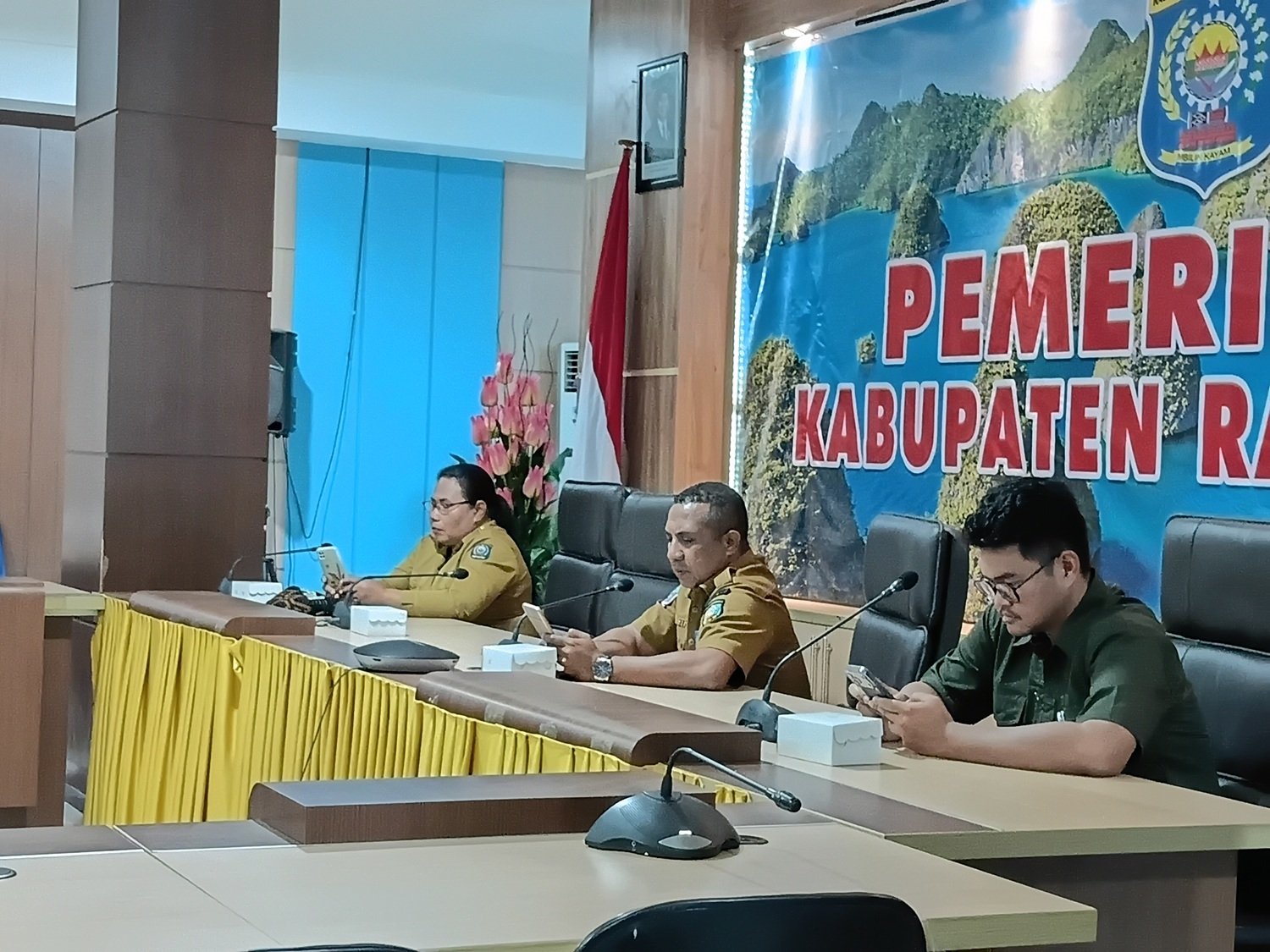 Ket: Kepala Dinas Tenaga Kerja dan Transmigrasi Kabupaten Raja Ampat, Marthen Luther R. Bartholomeus, ST., M.Si (tengah) didampingi Kepala Inspektorat Kabupaten Raja Ampat Martha Sanadi,S.Pd, M.Si (kiri) dan Kepala Kantor Cabang BPJS Ketenagakerjaan Raja Ampat Fahd Afkar Hakiki (kanan) mengikuti zoom meeting Rapat Koordinasi, Asistensi, dan Monitoring Evaluasi Capaian Universal Coverage Jaminan Sosial Ketenagakerjaan (UCJ) serta Diseminasi UCJ Award Tahun 2026 yang diselenggarakan Direktorat Jenderal Bina Pembangunan Daerah Kementerian Dalam Negeri bersama BPJS Ketenagakerjaan secara daring di Aula Wayag, Kantor Bupati Raja Ampat, Selasa (28/7/2026)/Foto: Bagian Prokopim Setda Raja Ampat